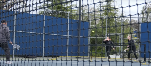Three people seen through a black tennis net playing pickleball on the College of the Canyons Campus.